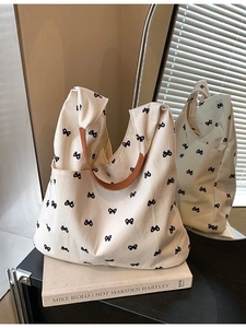Chic cream canvas tote bag with black bow patterns and brown leather handles