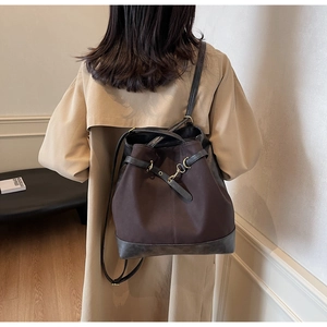 Detail view of large dark brown bucket bag with drawstring on beige trench coat
