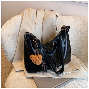 Close-up of black PU leather shoulder bag with plush bear charm and checkered ribbon decor
