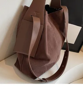 Close-up of brown suede bucket bag with smooth leather strap and detailed side stitching