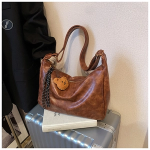 Brown vintage leather dumpling bag detail with cute plush bear charm and woven tassel