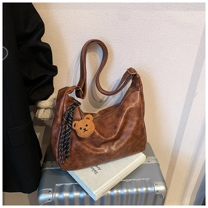 Detail view of brown leather hobo bag with teddy bear charm and striped tassel detail