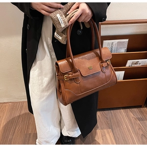 Brown retro leather shoulder bag with gold buckle detail and brand logo in a work setting
