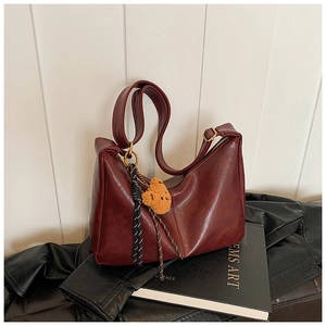 Detail of burgundy leather dumpling bag with plush bear charm and long shoulder strap