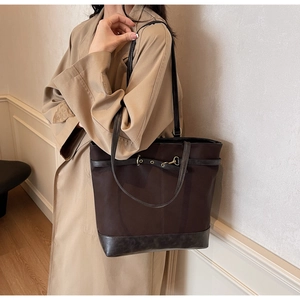 Detail of dark brown tote bag with metal buckles worn over a khaki trench coat