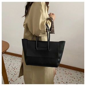 Close-up of a black matte leather tote bag with thin handles on a trench coat model