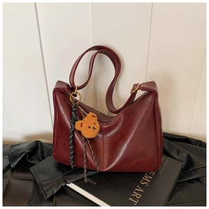 Detail of burgundy leather hobo bag with plush bear charm and woven rope decoration