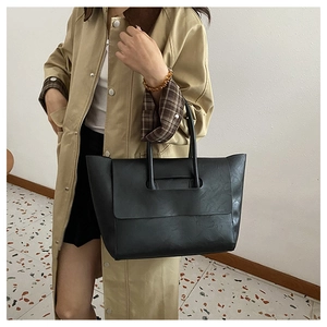 Detail of minimalist black tote bag with unique curved handle on a stylish commute outfit