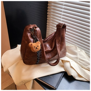 Detail of retro brown leather shoulder bag with a cute plush bear charm on soft fabric