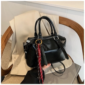 Sac Boston en cuir huilé noir brillant avec pendentif posé sur une chaise en bois