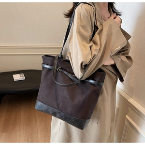 Detail of a large brown canvas tote bag with leather trim and gold buckle detail
