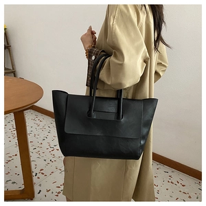 Detail of minimalist black tote bag with unique handle slot on textured matte leather