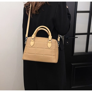 Back view of model in black suit carrying a light brown quilted leather Boston handbag