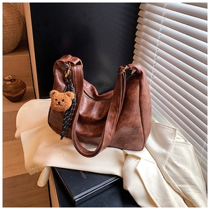 Detail of a brown vintage half-moon bag with a cute plush bear charm on white suit