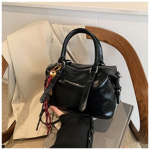 Détail du sac Boston noir brillant avec charme tressé rouge et blanc sur fond de costume chic