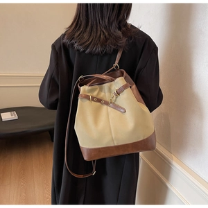 Detail of contrast stitching canvas and brown leather bucket bag with metal buckle straps