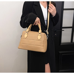 Close-up of beige quilted tote bag with crosshatch texture on black coat model