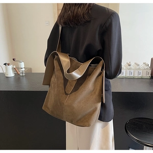 Detail of dark brown suede tote bag with smooth leather strap worn by a model