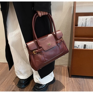 Detail of burgundy leather shoulder bag with gold hardware buckle and brand logo