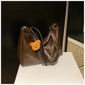 Detail of dark brown dumpling bag in glossy leather with a plush bear pendant charm