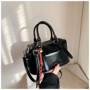 Détail du sac Boston noir brillant avec ferrures dorées et breloque en cordon rouge
