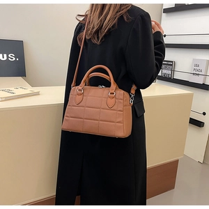 Brown quilted leather tote bag with round handles and adjustable shoulder strap worn by model
