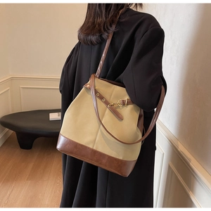 Detail of a khaki canvas bucket bag with brown leather trim and golden metal hook closure