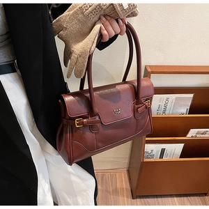 Detail of burgundy leather tote featuring gold brand plaque and textured flap design