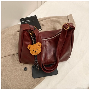 Detail of burgundy leather tote bag with gold hardware and plush bear charm on a suit