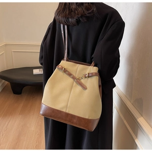 Detail of khaki canvas tote with brown leather trim and metal hook buckle on model