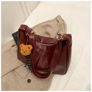 Detail of burgundy glossy PU leather bag with wide strap and cute plush bear charm