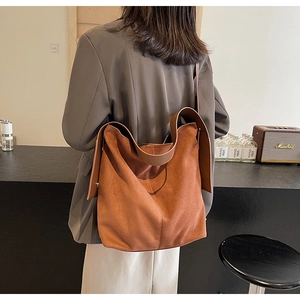 Back view of a large brown suede tote bag worn by a model in a cozy cafe setting
