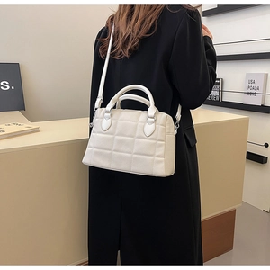Detail of a creamy white quilted tote bag worn by a model in a minimalist modern setting