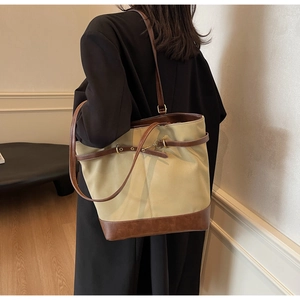 Model wearing large khaki canvas and brown leather tote bag in a home setting