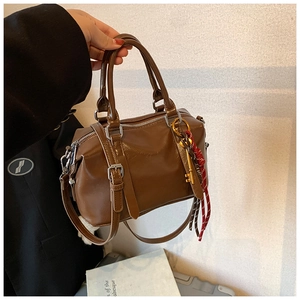 Détail du sac Boston marron avec breloque clé dorée et sangle à rayures décorative