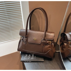 Close-up of retro dark brown leather tote bag featuring a gold logo and metal buckle detail