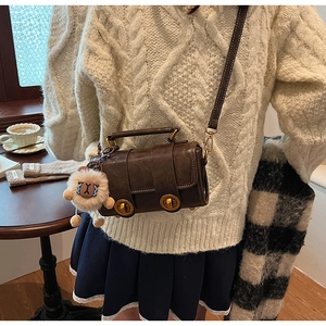 Détail du sac bandoulière en cuir marron foncé avec boucles dorées et breloque agneau
