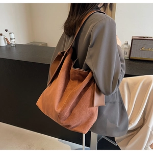 Detail of dark brown suede bucket bag worn by model in a cozy cafe setting