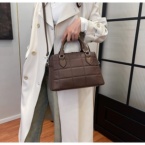 Brown quilted Boston bag held by model in white trench coat, showing side profile and texture
