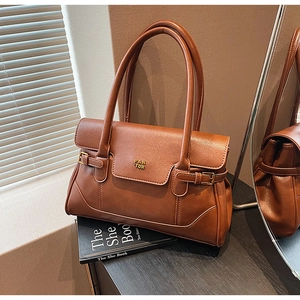 Detailed shot of brown lychee-textured leather bag with golden logo and buckle accents
