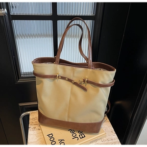 Detail of a large khaki tote bag with dark brown leather straps and gold buckle buckle