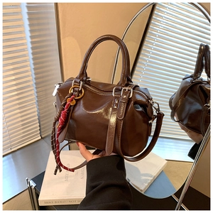 Détail d'un sac Boston marron avec quincaillerie argentée et breloque en corde tressée
