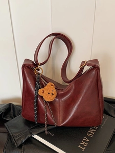 Retro dark red dumpling bag with teddy bear charm and woven tassel on white backdrop
