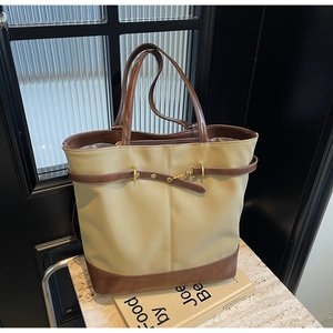 Detail of a large two-tone tote bag with beige fabric, brown leather trim and gold buckle