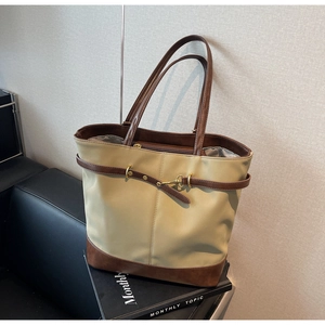 Detail of khaki canvas tote with dark brown leather straps and metal buckle closure