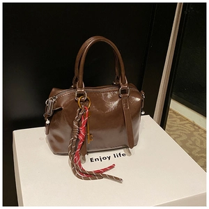 Détail du sac polochon rétro marron brillant avec nœud tressé et breloque clé dorée