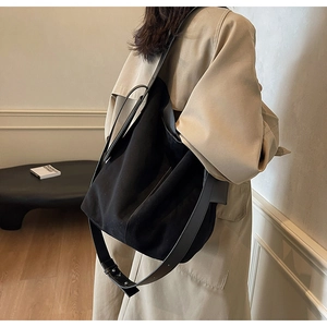 Black canvas shoulder bag with wide strap styled with a classic beige trench coat