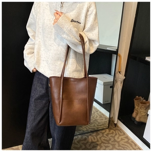 Brown leather tote bag featuring a vintage bucket design and wide shoulder strap