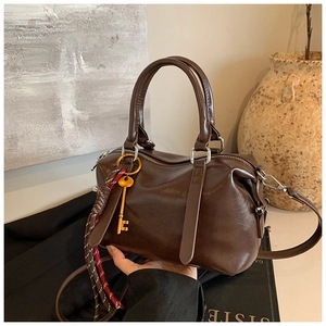 Détail du sac Boston en cuir ciré marron avec breloque clé dorée et sangle tissée