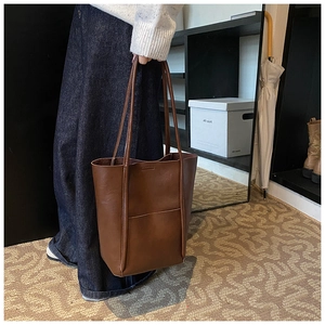 Close-up of brown leather bucket tote bag showing detailed texture and external pocket